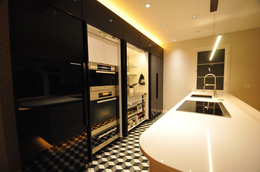 Modern kitchen with sleek black cabinetry, stainless steel appliances, and stylish chevron flooring.