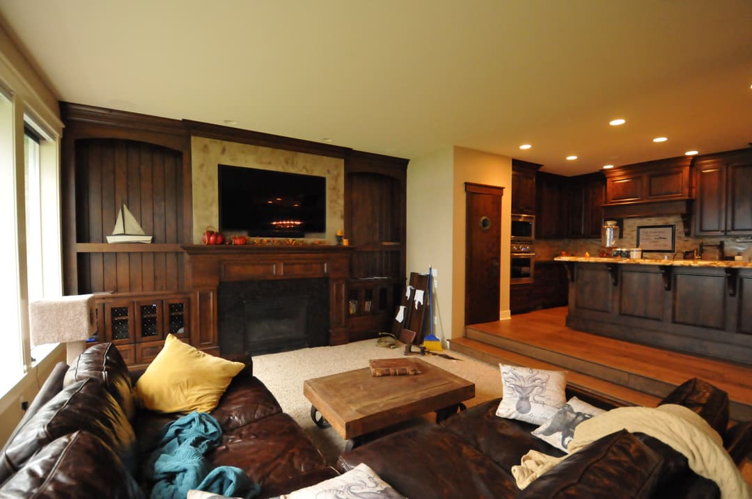 Cozy living room with dark wood accents, leather couches, and modern kitchen in the background.