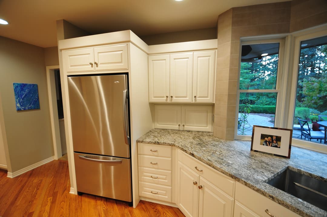 Modern kitchen featuring stainless steel refrigerator, granite countertops, and natural light.