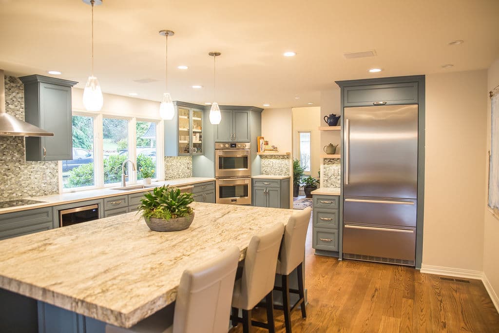 Modern kitchen with blue cabinets, marble island, stainless steel appliances, and natural light.