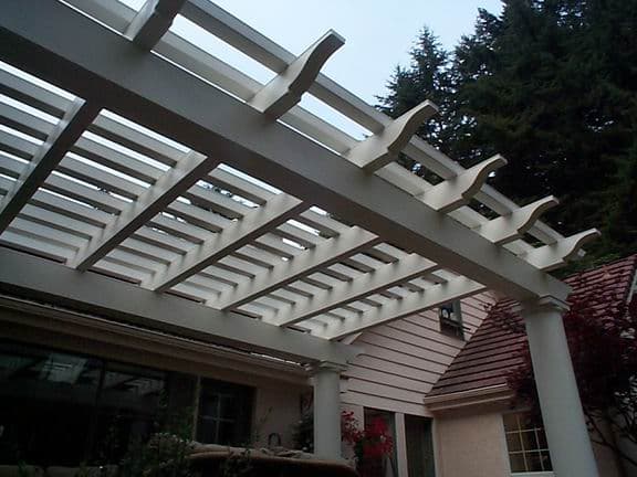 White wooden pergola with columns, viewed from below, in a residential backyard setting.