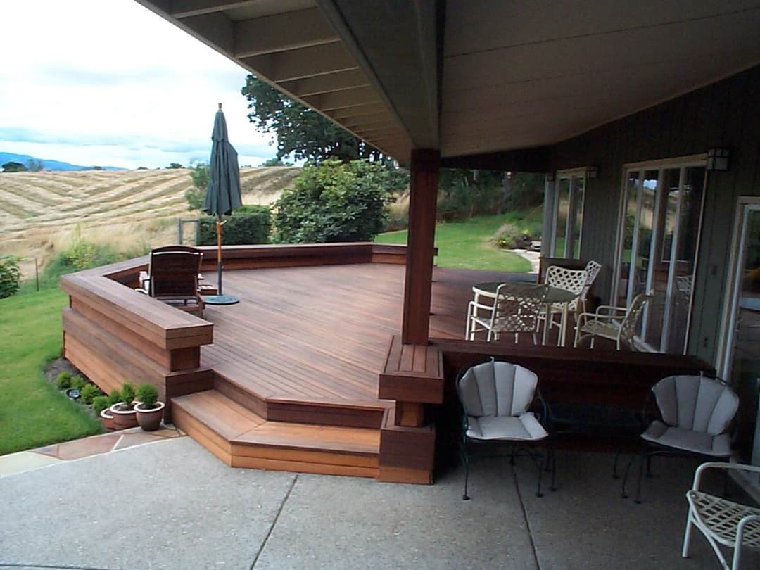 Spacious wooden deck with seating, umbrella, and scenic view of fields and hills.