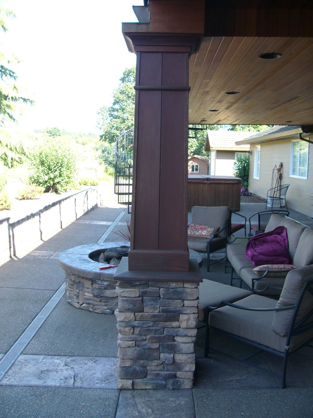 Cozy outdoor seating area with stone fire pit and wooden posts, surrounded by greenery.
