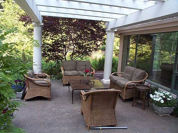 Cozy outdoor patio with wicker furniture, lush greenery, and a glass table for relaxation.