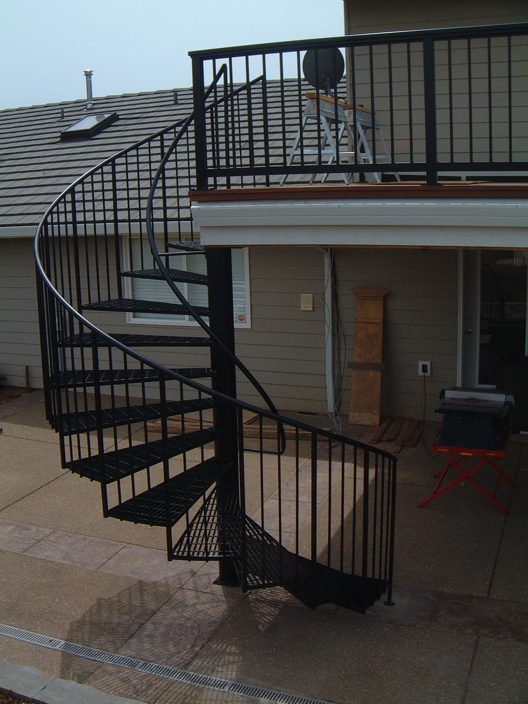 Spiral black metal staircase leading to a deck on a modern house exterior.