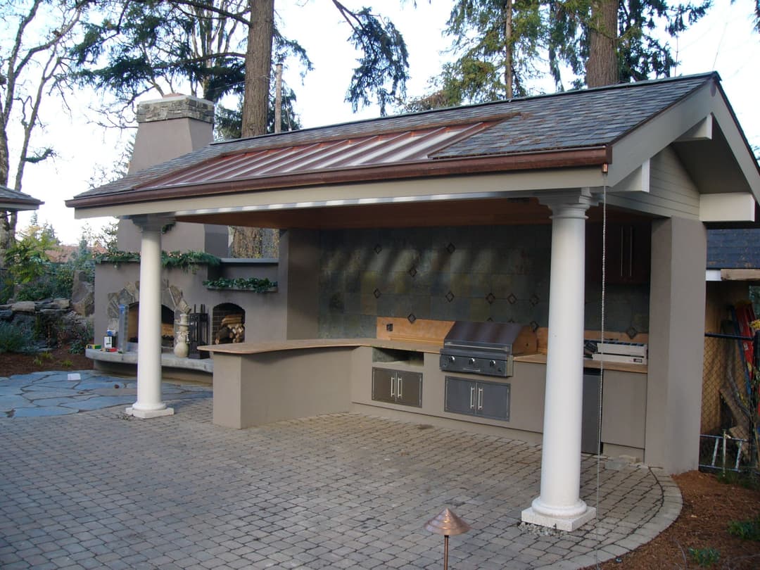 Outdoor kitchen with grill, stone fireplace, and modern design under a covered patio.