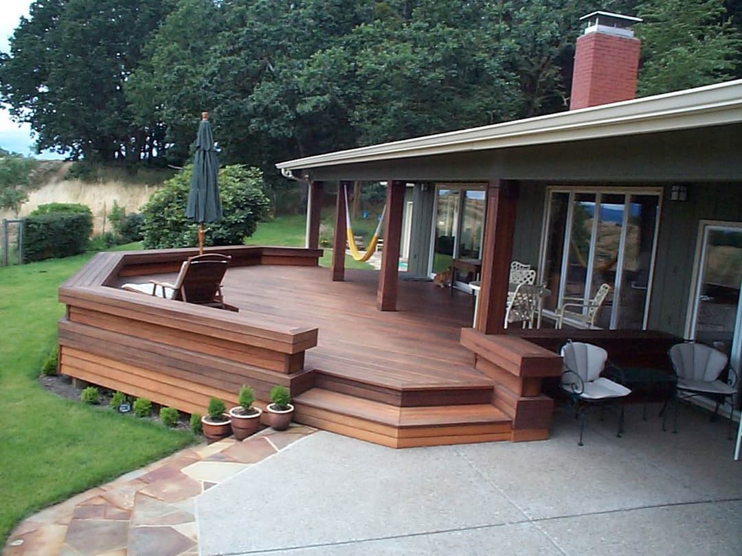 Modern wooden deck with seating area and garden, featuring a hammock and umbrella in a tranquil setting.