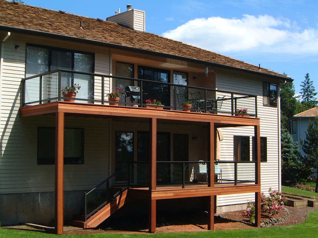 Modern home with a wooden deck, railing, and flowering pots under a blue sky.