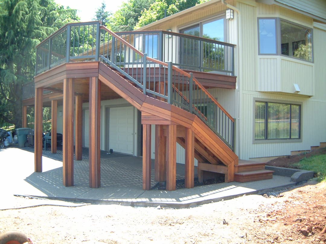 Wooden outdoor staircase leading to a deck, surrounded by greenery and a modern home.