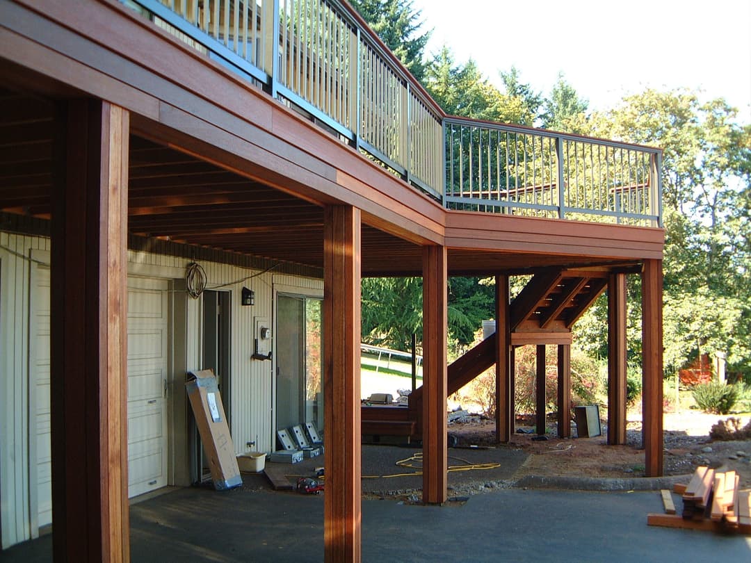 Wooden deck with railing and stairs, surrounded by greenery and home exterior.