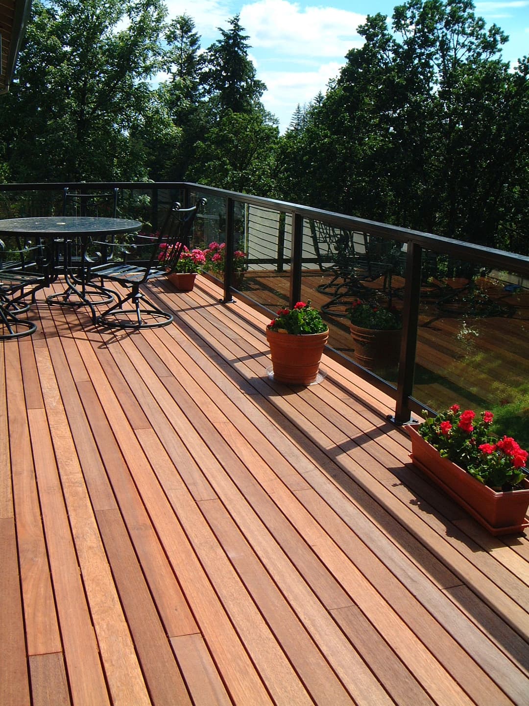 Wooden deck with potted flowers, outdoor seating, and a view of surrounding trees.