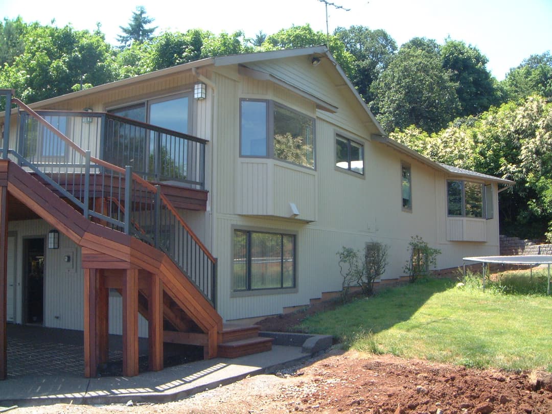 Modern home exterior featuring wooden stairs and lush greenery in the background.