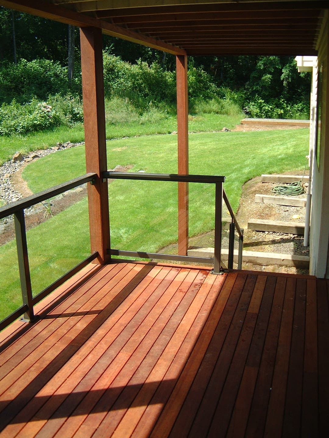 Wooden deck with glass railing, leading to a well-maintained grassy yard. Sunny day backdrop.