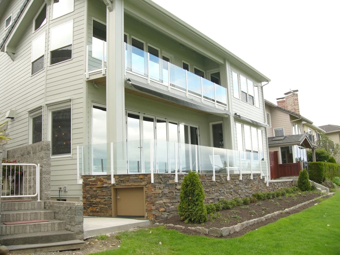 Modern waterfront home with glass railing balcony and stone accents in landscaped yard.
