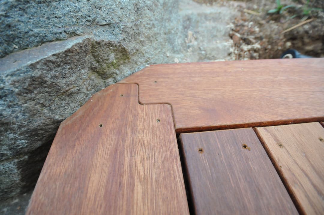 Detailed close-up of wooden decking corner joint next to a rock surface.