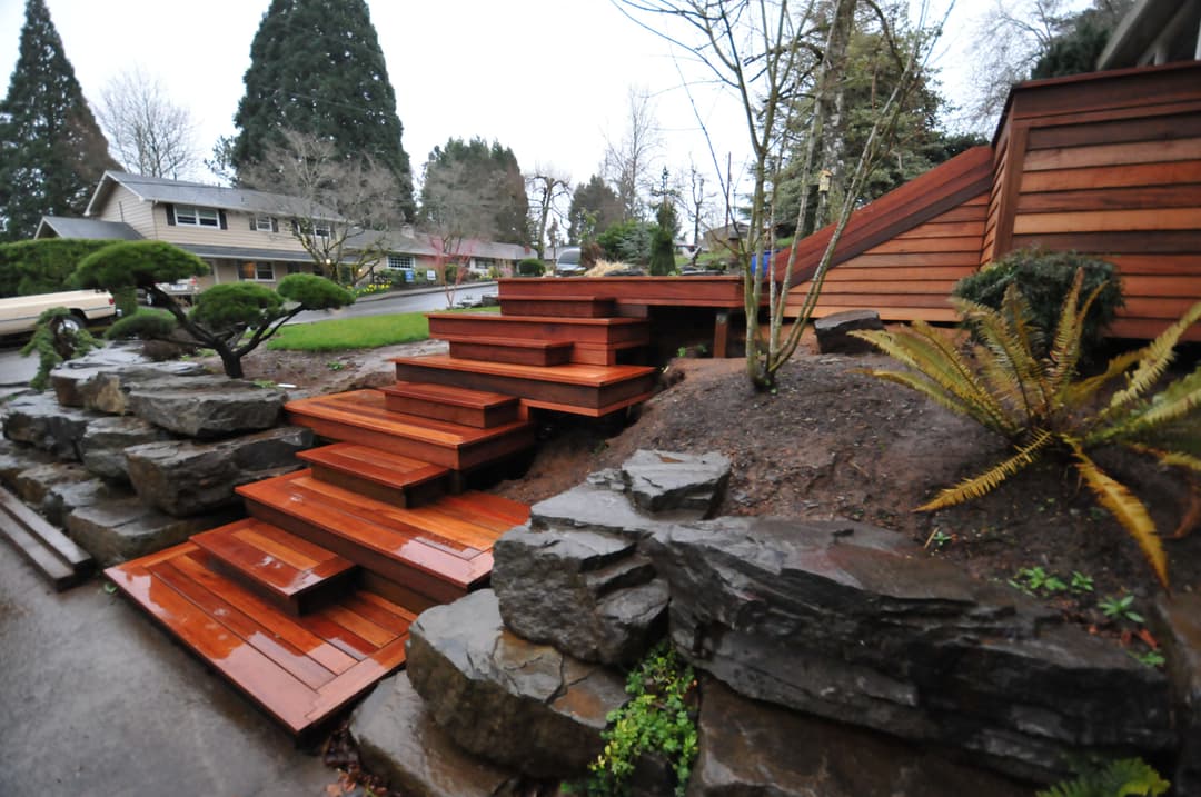 Elegant wooden steps leading through a landscaped garden with rocks and greenery.