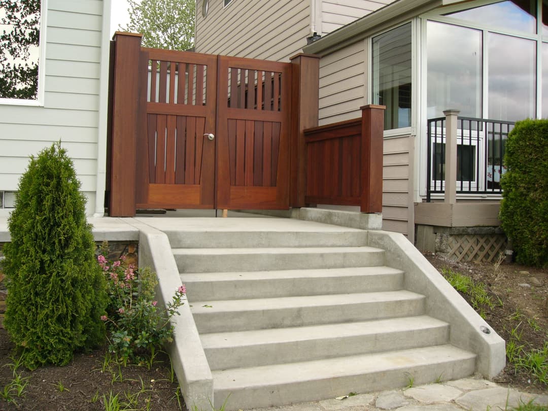Elegant wooden gate with vertical slats at the entrance, leading up to concrete steps and a modern home.