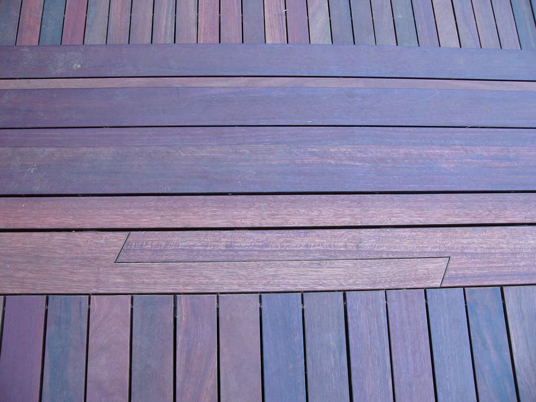 Wooden deck flooring with varying shades of purple and brown planks arranged in a pattern.