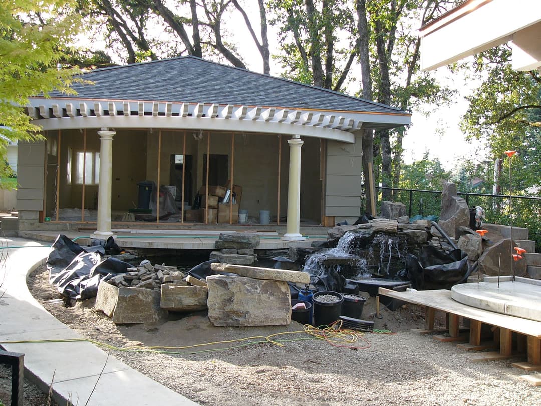 Residential outdoor space featuring a stone waterfall, patio area, and nearing completion landscaping.