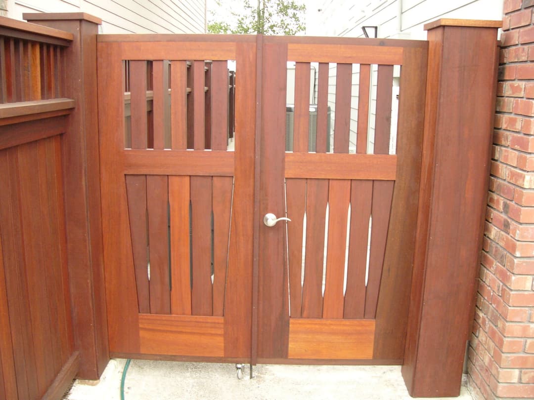 Wooden garden gate with vertical slats and a metal handle, surrounded by a fence.