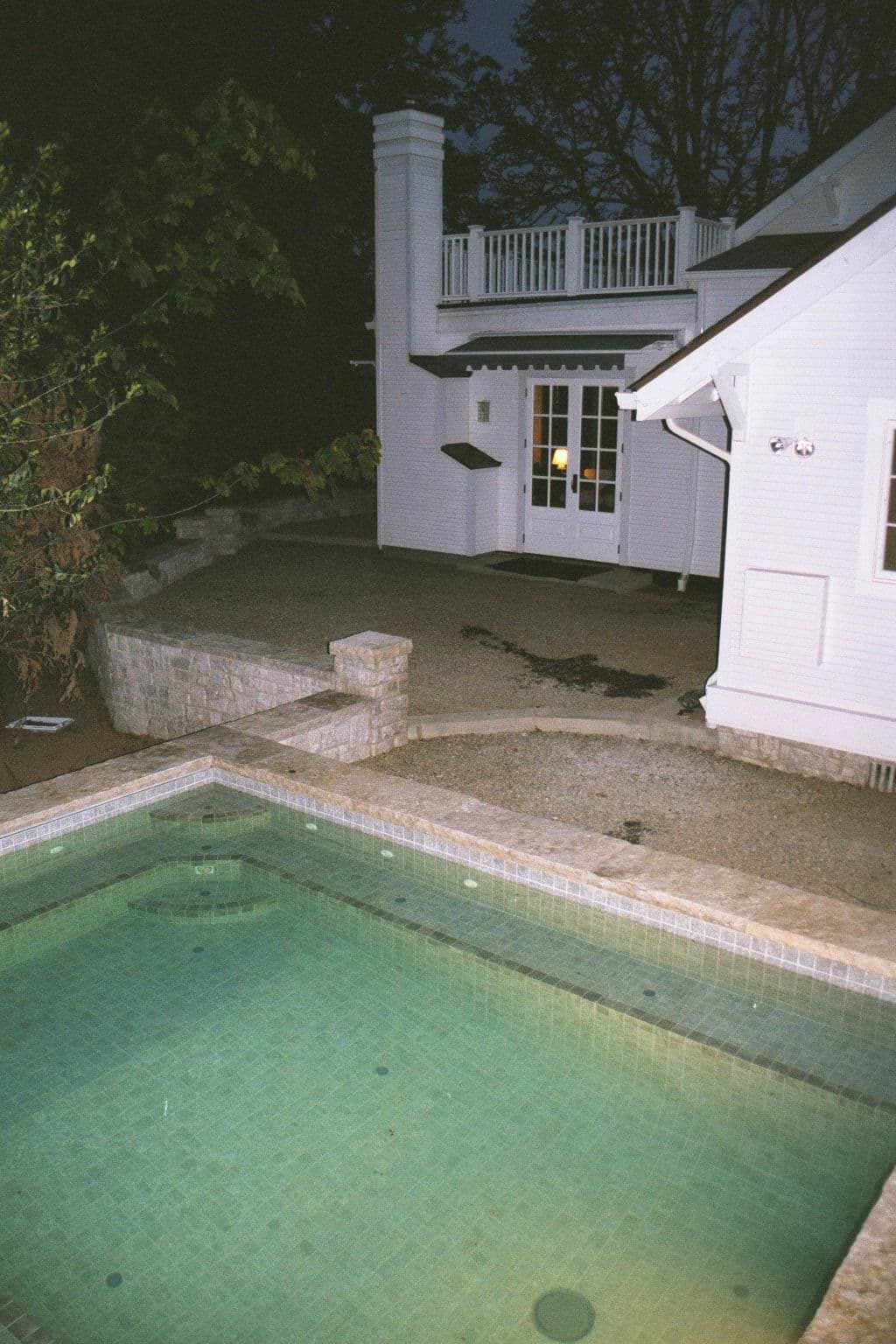 Evening view of a peaceful pool area beside a white house with patio and outdoor furniture.