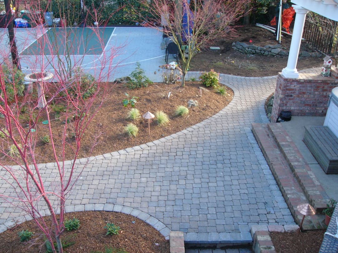 Scenic backyard pathway with paver stones, landscaped plants, and outdoor recreational areas.
