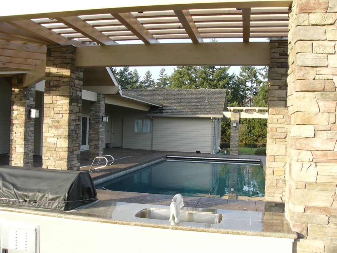 Luxurious backyard with a stone patio, swimming pool, and modern outdoor kitchen area.