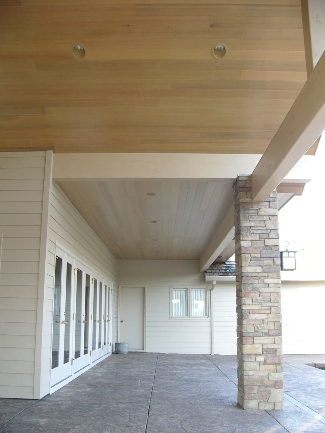 Modern home entryway with wooden ceiling, stone pillar, and glass doors.
