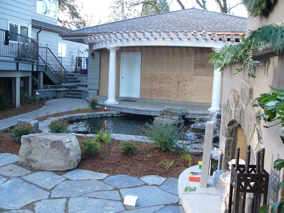 Renovated backyard with pond, stone pathway, and new porch under construction.