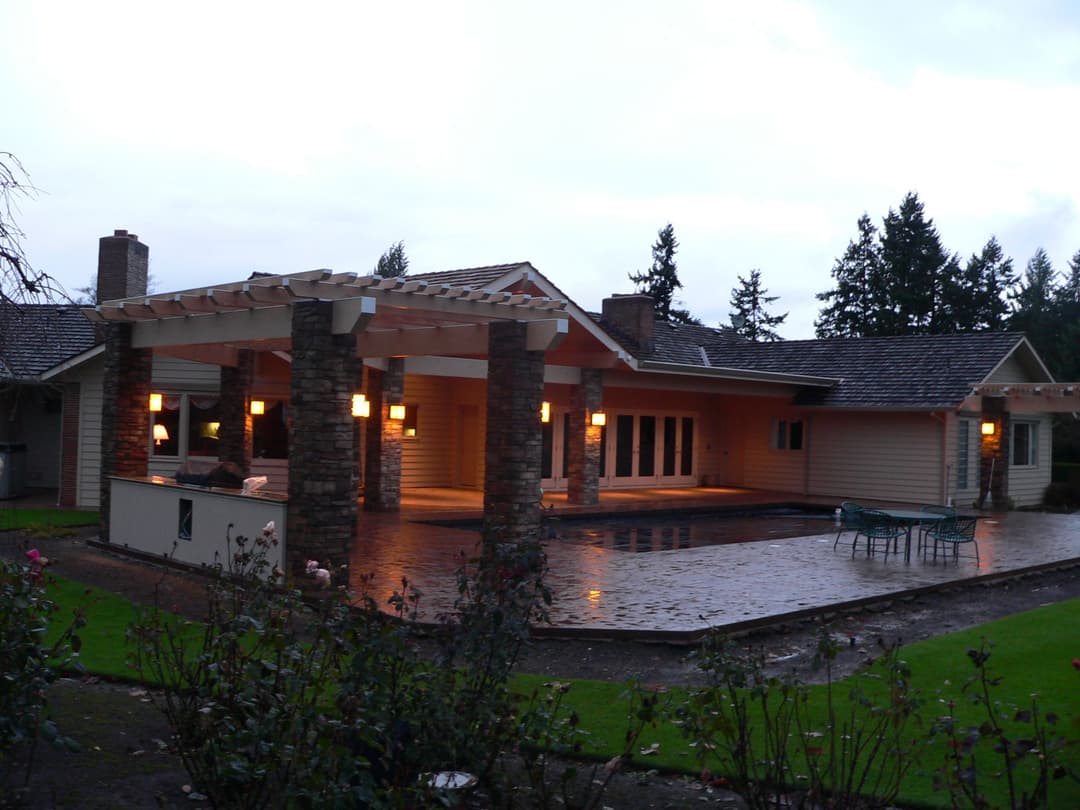 Modern home exterior with stone columns, pool, and landscaped yard at dusk.