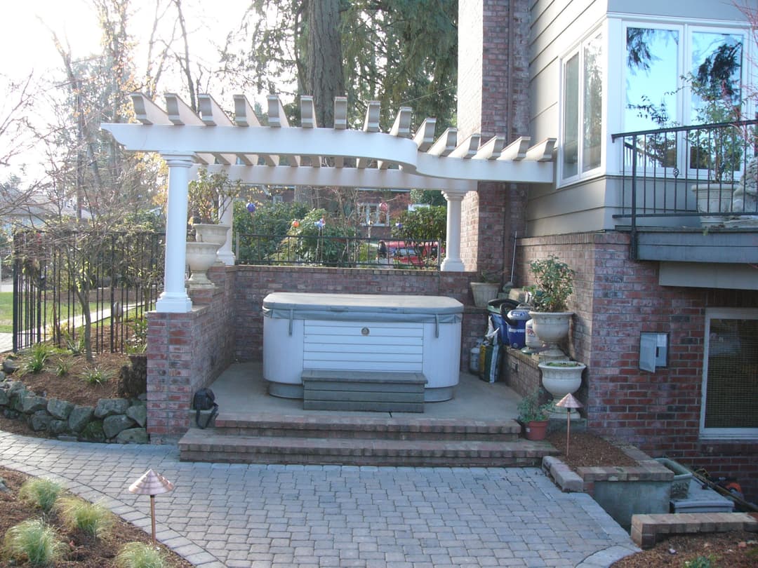 Backyard patio with a hot tub, brick walls, and a pergola surrounded by landscaping.