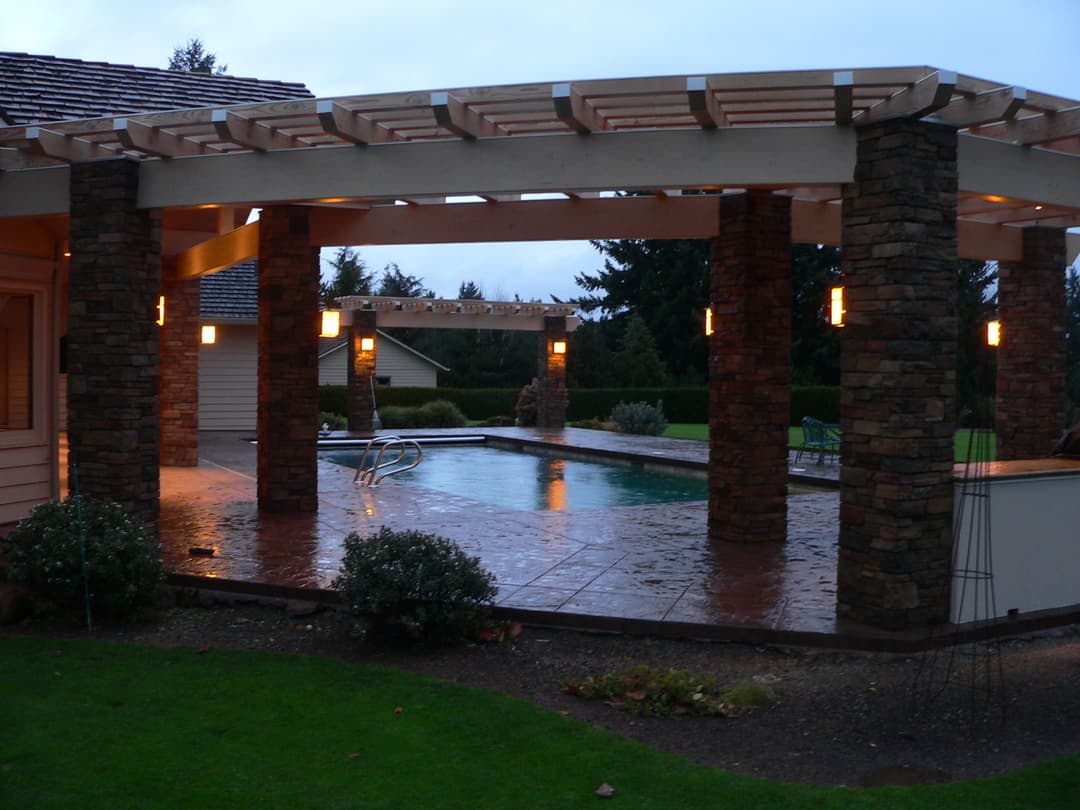 Modern outdoor patio with a pool surrounded by stone pillars and soft lighting.