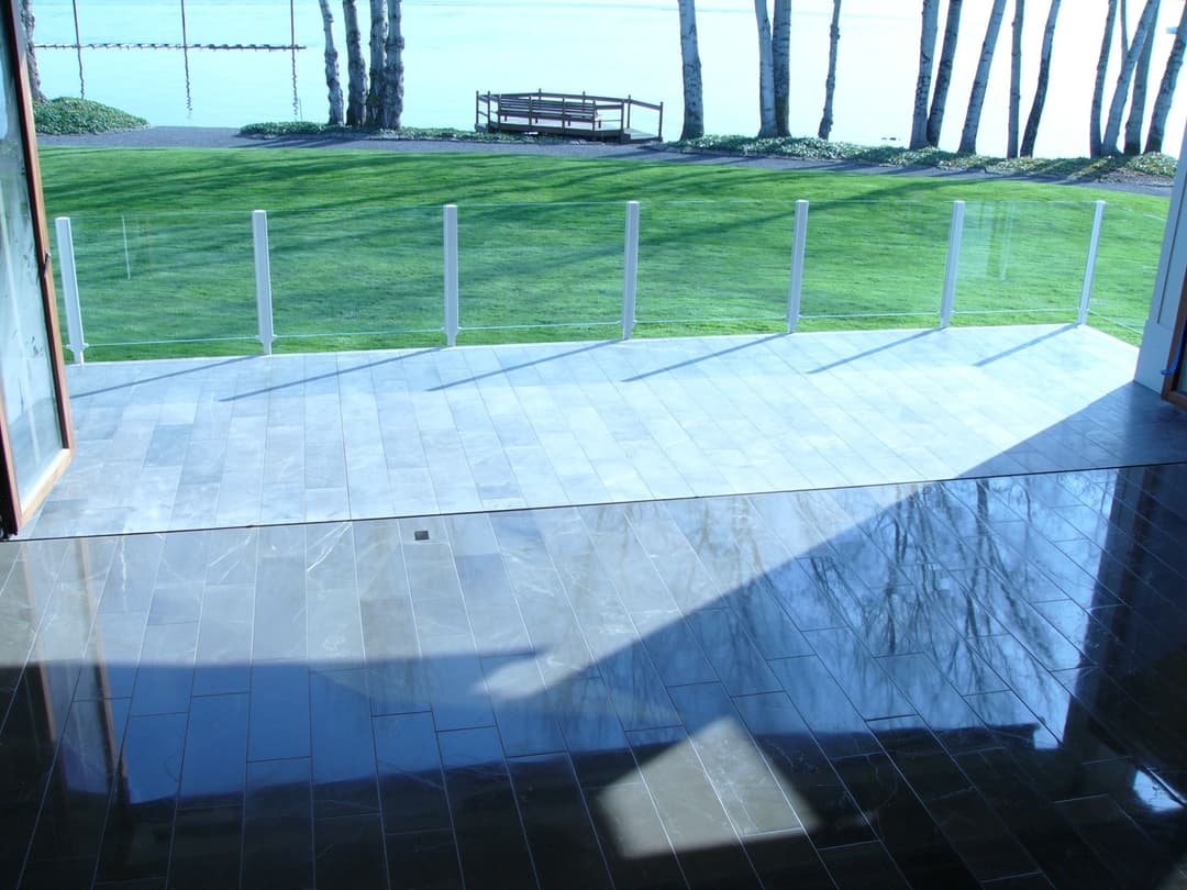 Modern glass balcony overlooking a tranquil green lawn and calm waterway.