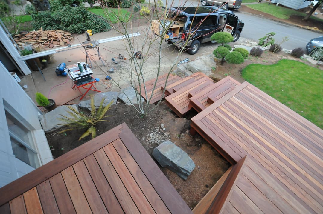 Modern wooden deck installation with tools and landscaping in a residential yard.