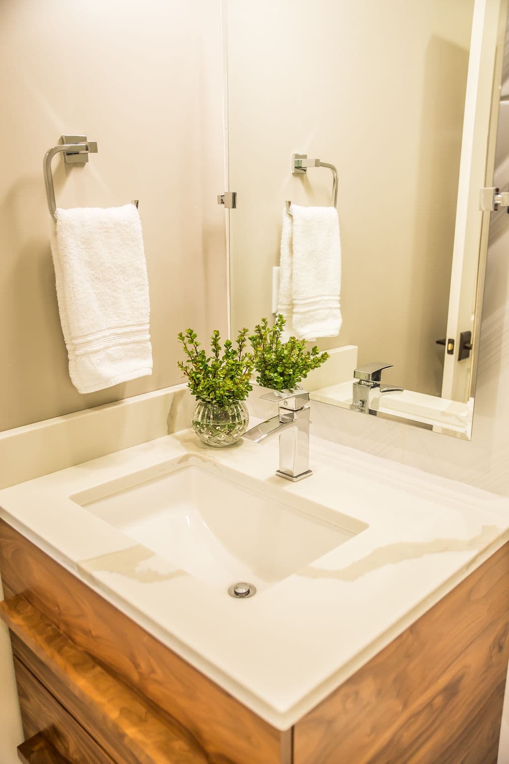 Modern bathroom sink with wooden vanity, white towels, and a decorative plant.