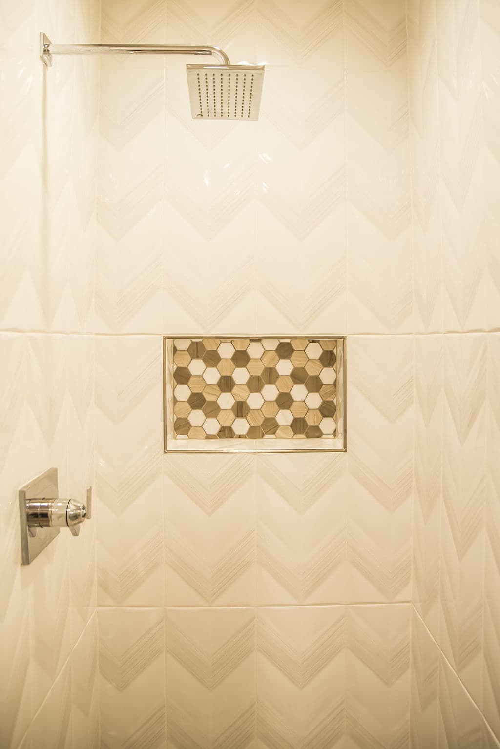 Modern shower with chevron tile design and a hexagonal niche for storage.