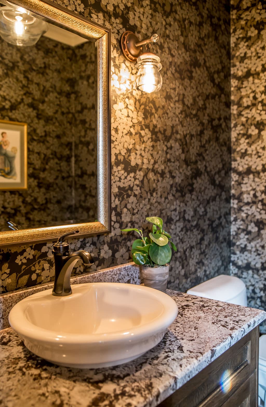 Beautiful bathroom with floral wallpaper, vintage mirror, and elegant sink with a plant.