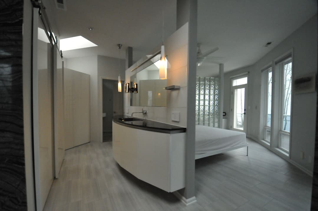 Modern bedroom with curved vanity, natural light, and glass block wall. Stylish and spacious design.