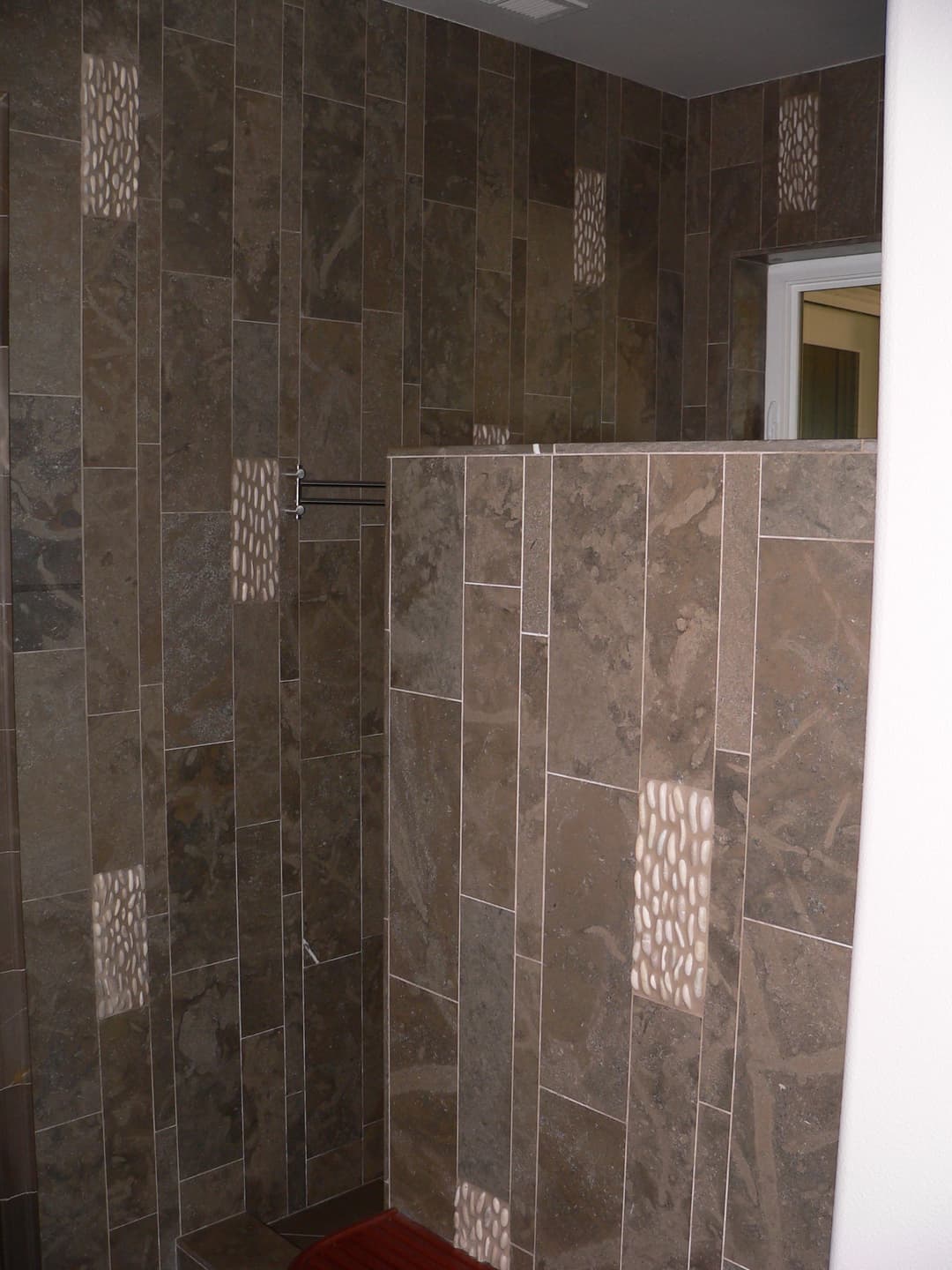 Modern shower with natural stone tiles and unique decorative accents. Stylish bathroom design.