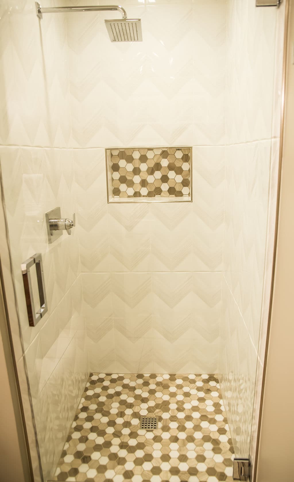 Modern shower design with hexagon tile accent and glass enclosure. Elegant chevron wall pattern.
