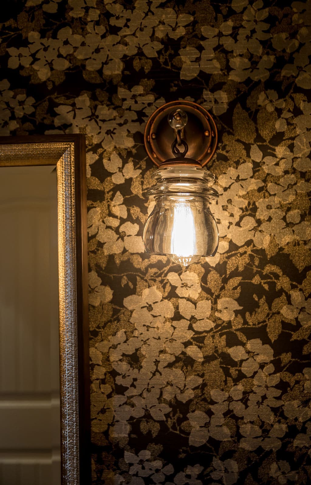 Vintage jar light fixture against floral wallpaper with a mirror reflection.