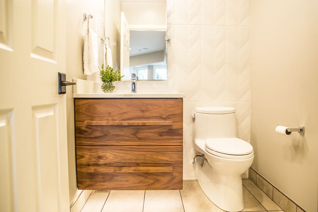Modern bathroom with wooden vanity, white toilet, and stylish tile accents. Bright and inviting.