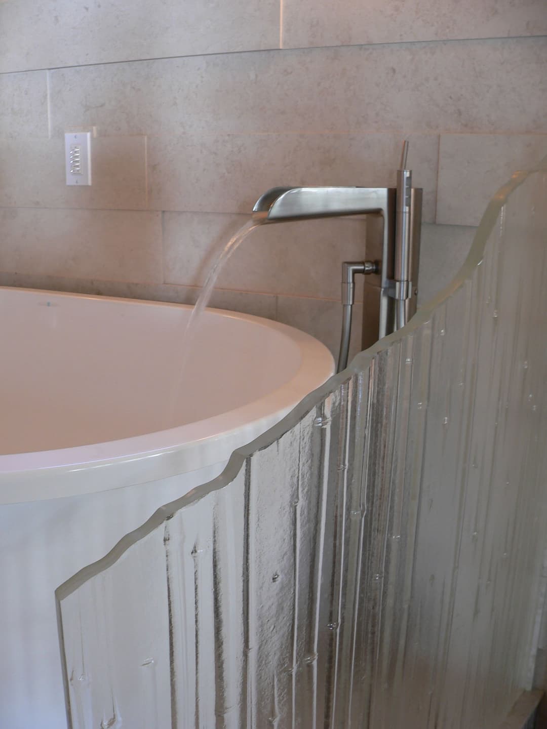 Modern bathtub with a sleek faucet and textured glass partition, in a minimalist bathroom.