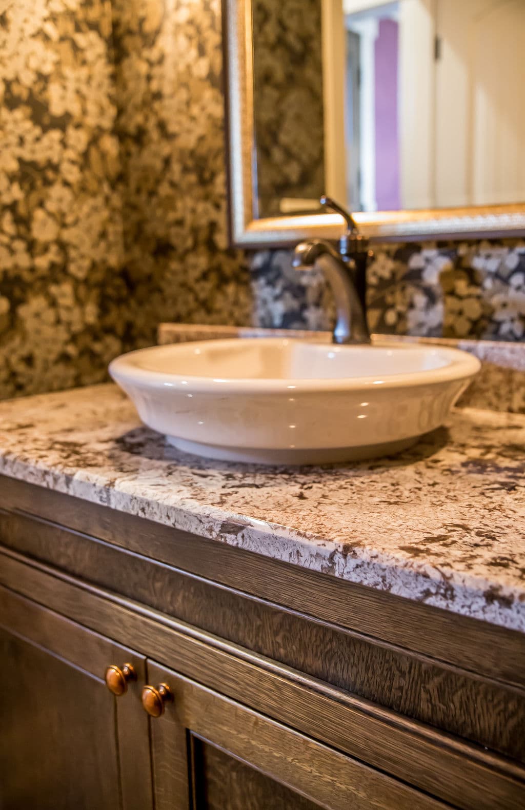 Elegant bathroom sink with decorative countertop and ornate mirror, showcasing floral wallpaper.