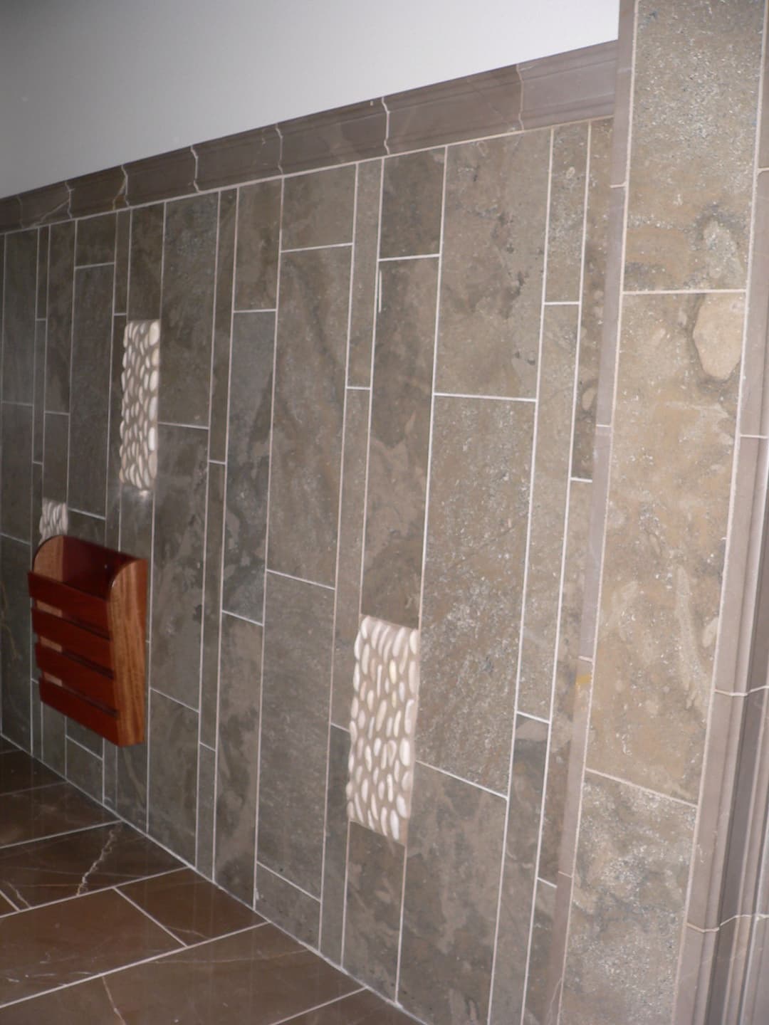 Textured stone wall with integrated wood shelving and contrasting tile patterns. Modern interior design.