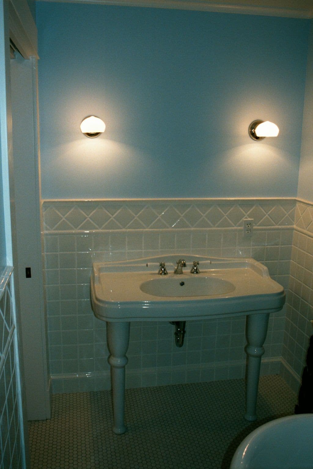 Vintage bathroom with blue walls, white tiled sink, and elegant wall sconces.