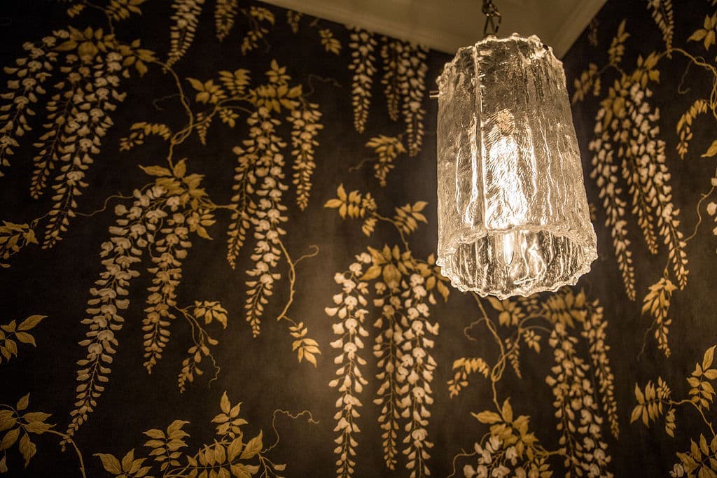 Elegant glass pendant light against floral wallpaper with gold and white designs.