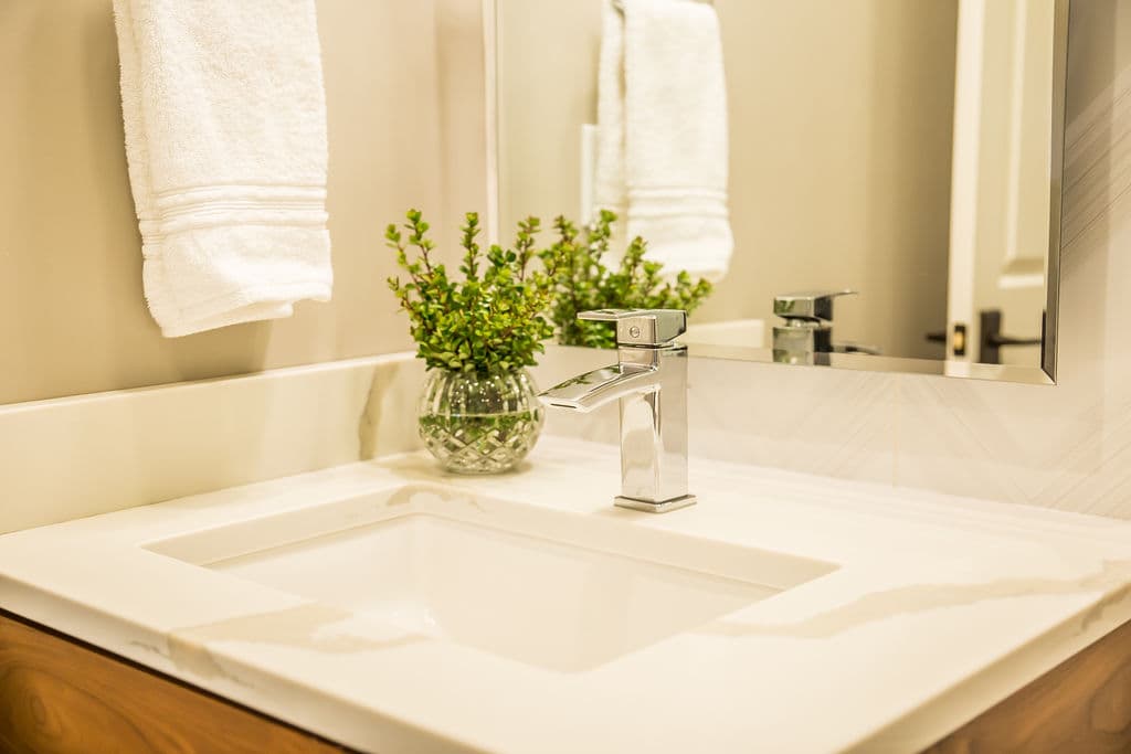 Modern bathroom sink with chrome faucet, white towels, and decorative greenery in glass vase.