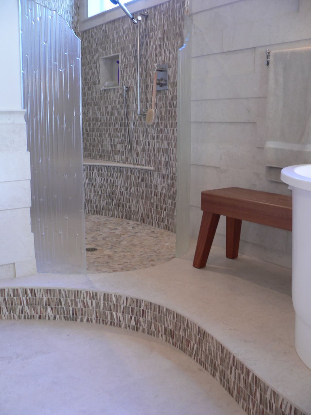 Modern bathroom featuring a spacious walk-in shower, elegant tile work, and a wooden bench.