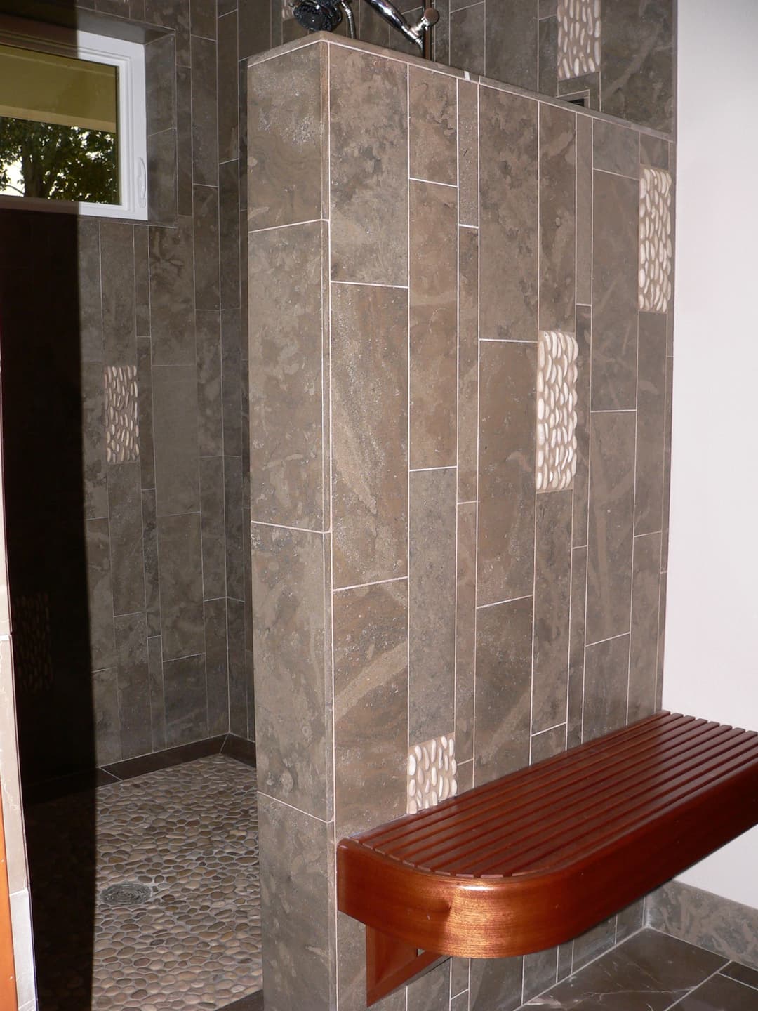 Modern shower featuring textured tile walls and a wooden bench for comfort.